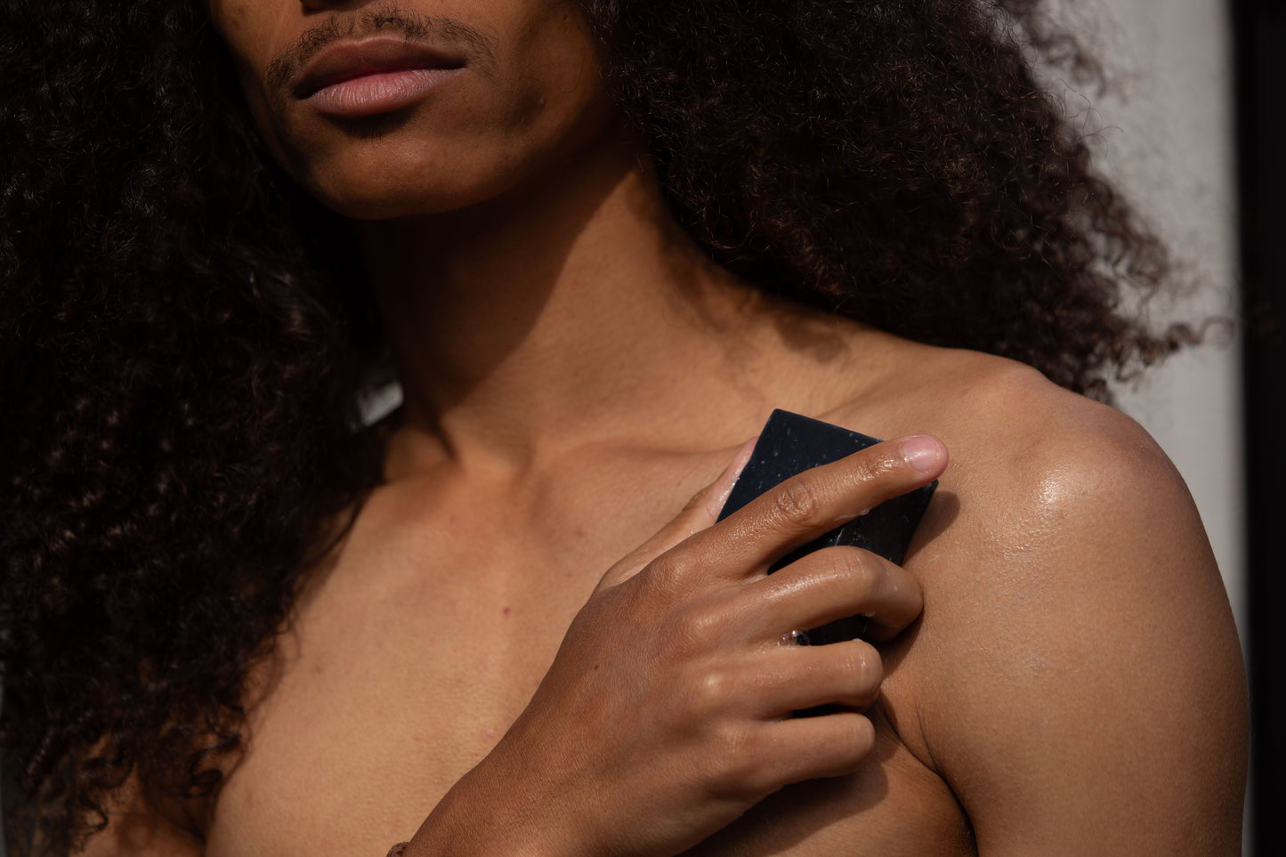 A close-up of a person applying the black activated charcoal soap bar to their shoulder, emphasizing the natural skincare use of the "Butter & Lye" product.