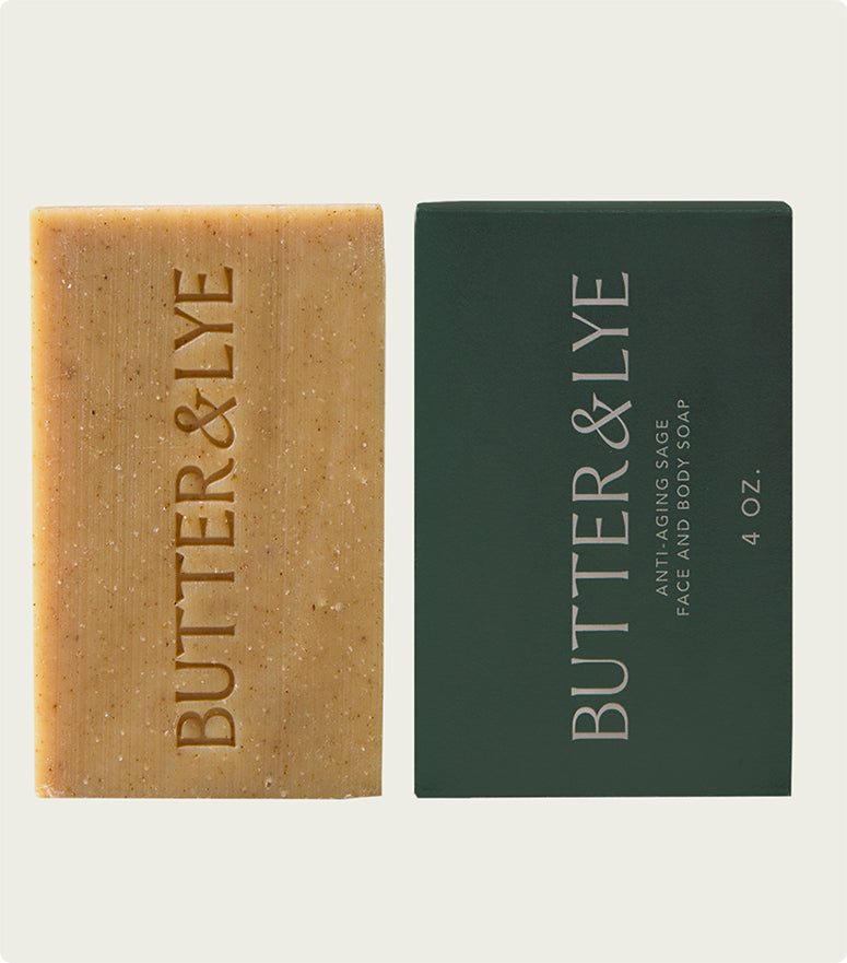 Two rectangular soap bars side-by-side. On the left is a close-up of a bar of soap, light golden brown in color, with "Butter & Lye" embossed in capital letters. On the right is a dark green rectangular box with "Butter & Lye" printed vertically in white letters. Below, in smaller letters, it reads "anti-aging sage face and body soap 4 oz."