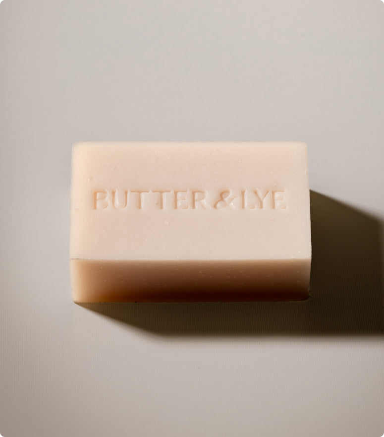 A simple, minimalist image of a light colored bar of soap bar embossed with Butter & Lye on it.