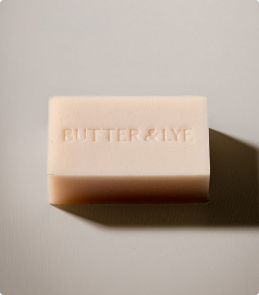 A simple, minimalist image of a light colored bar of soap bar embossed with Butter & Lye on it.