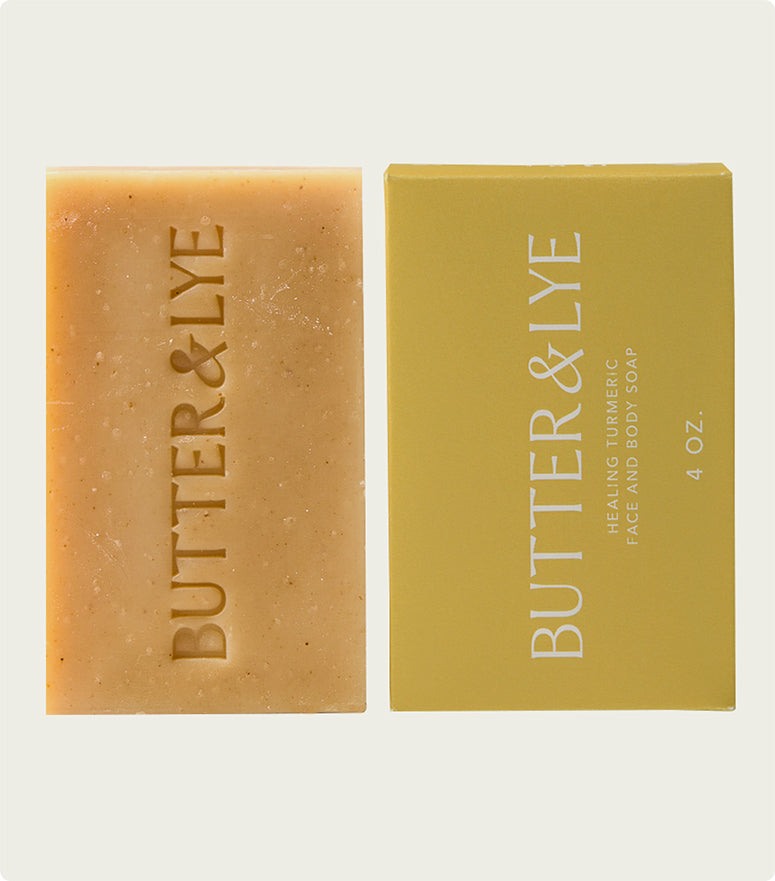 A single beige soap bar with "Butter & Lye" embossed, paired with its packaging. The box is a soft yellow and labeled "Healing Turmeric Face and Body Soap, 4 oz.
