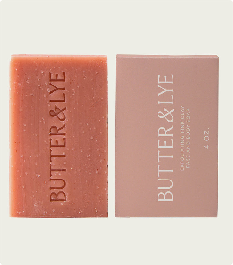 A flat-lay of a "Butter & Lye" pink soap bar next to its light pink packaging, labeled as a 4 oz bar, with a clean and sophisticated aesthetic.