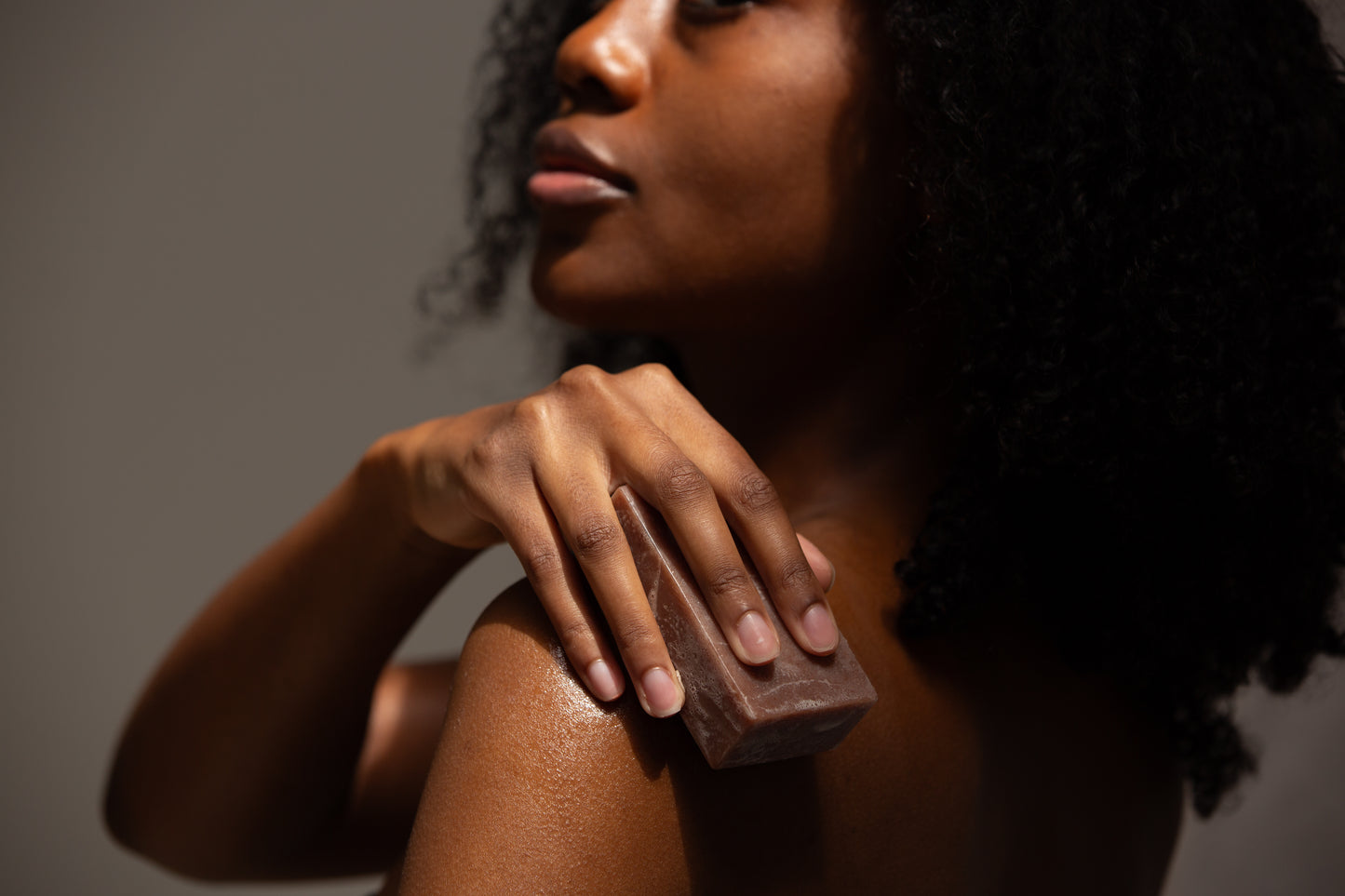 A woman gently applying the Butter & Lye soap bar to her shoulder, emphasizing the soap's moisturizing and soothing benefits for the skin.