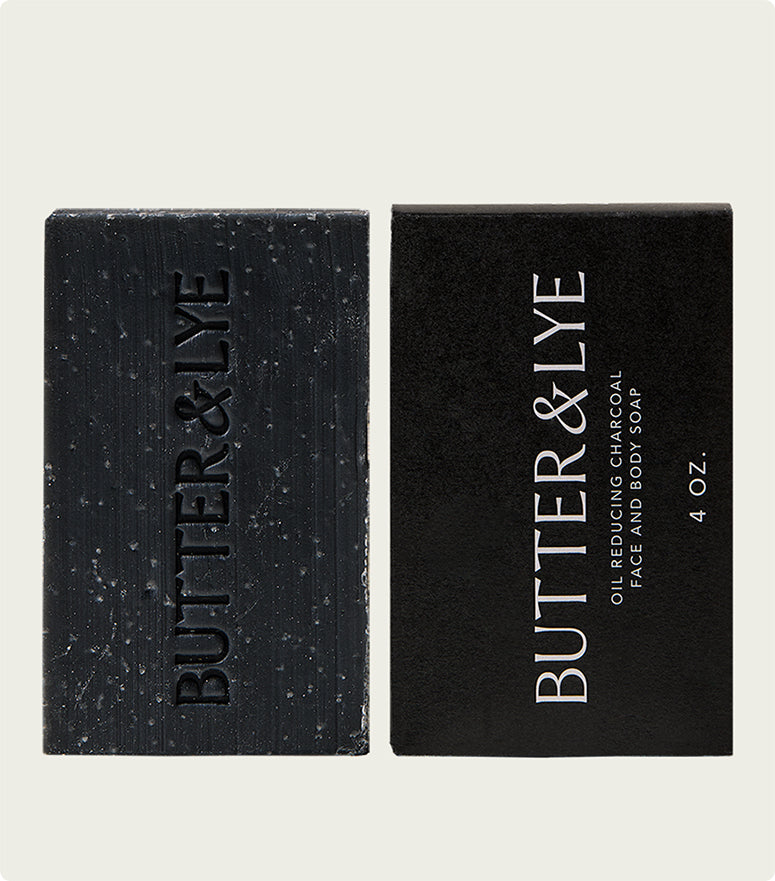 Two black charcoal soap bars placed vertically side by side, one showing the embossed "Butter & Lye" logo and the other displaying the product packaging with text reading "Oil Reducing Charcoal Face And Body Soap, 4 oz.”