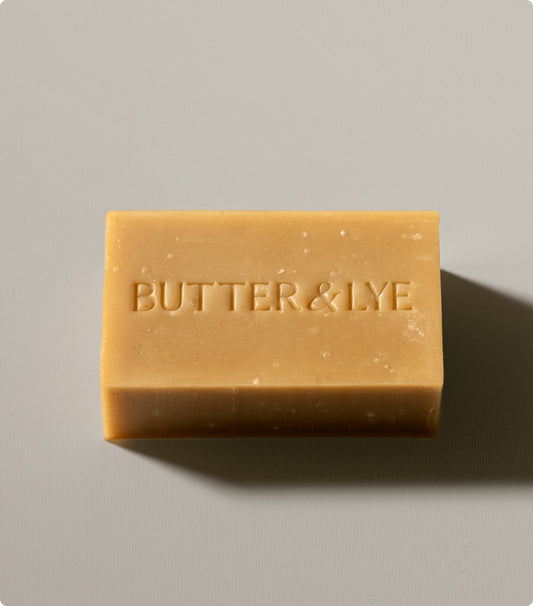 A close-up of a turmeric soap bar with 'Butter & Lye' engraved, showcasing its smooth, natural texture against a neutral background.