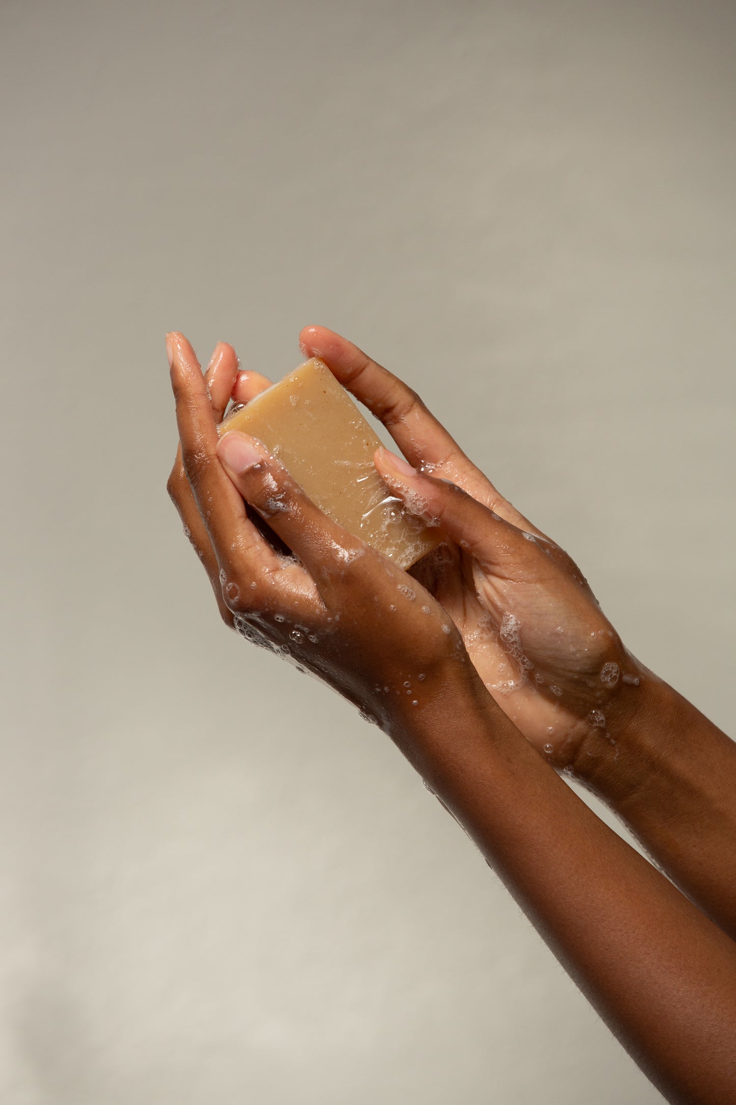 Hands lathering a Butter & Lye a soap bar with visible suds, illustrating the soap in use for skincare."