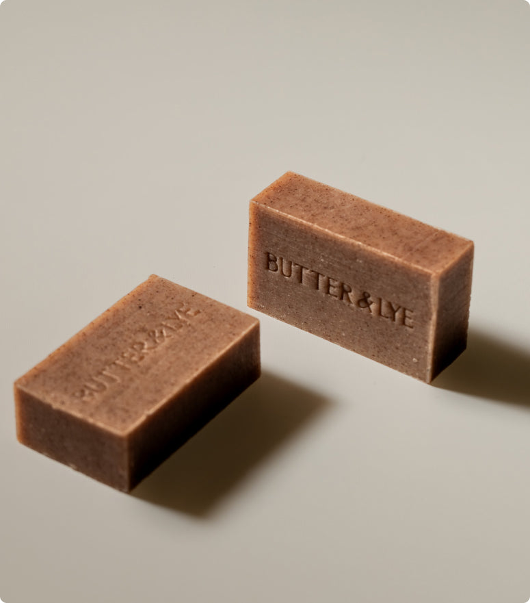 Two Butter & Lye rosehip soap bars displayed on a soft beige background, highlighting their natural texture and embossed logo.