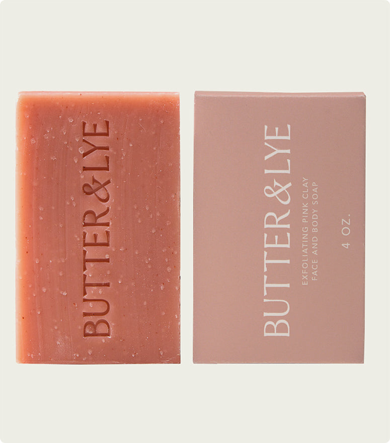  A flat-lay of a "Butter & Lye" pink soap bar next to its light pink packaging, labeled as a 4 oz bar, with a clean and sophisticated aesthetic.