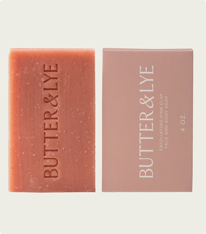  A flat-lay of a "Butter & Lye" pink soap bar next to its light pink packaging, labeled as a 4 oz bar, with a clean and sophisticated aesthetic.