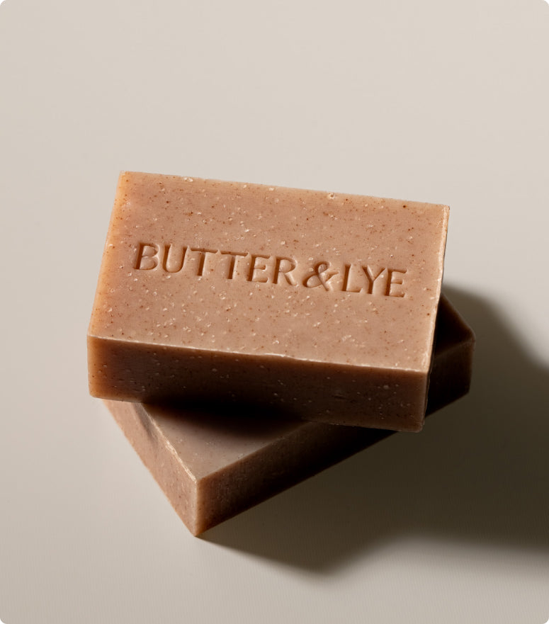 Two stacked bars of cinnamon soap engraved with 'Butter & Lye,' showcasing their natural speckled texture against a neutral background.