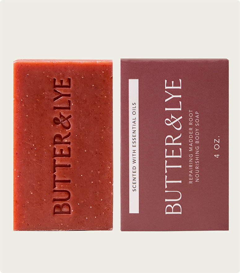 A Butter & Lye Repairing Madder Root soap bar next to its deep red packaging, featuring the brand name and product details in clean, minimalist design.